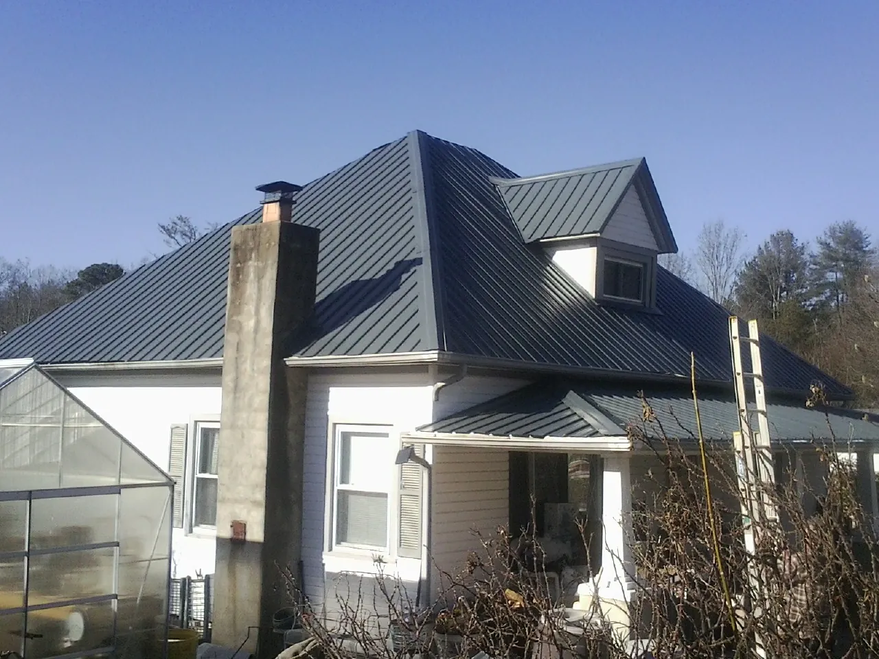 Dark blue standing seam metal roof on a white farmhouse with dormer — Slate & Tile Roof Repair by Roofing Brothers in Malden