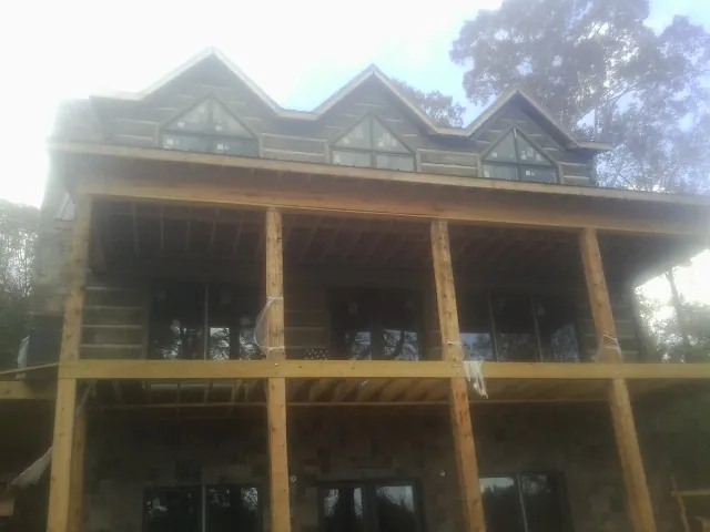Dormers and porch framing on a large log home under construction — Roof Coating work by our crew in Malden